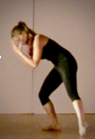 A woman bends over with arms to head, one leg outstreched along the floor.