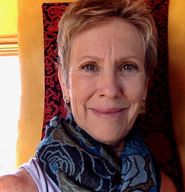 She is a white woman with close cropped light hair, smiling, and wearing a blue patterned scarf.