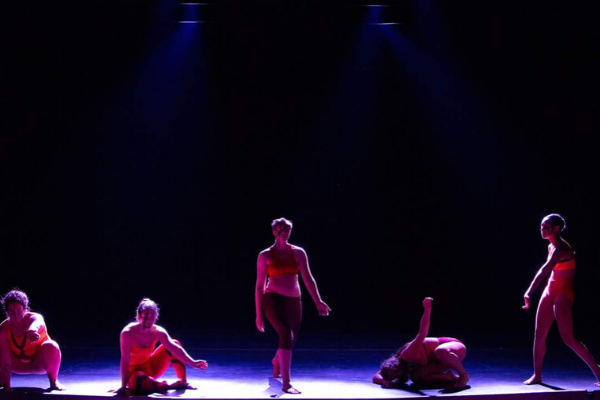 A group of dancers posed at different levels on stage against a black back round.