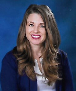 Meg is a white woman with light brown hair against a blue backround wearing a black jacket