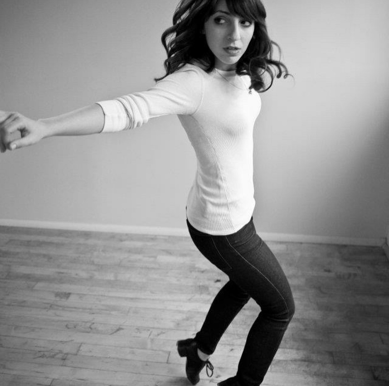 Debra is wearing a white shirt and jeans and is standing on her toes, she has dark hair and the photo is in black and white