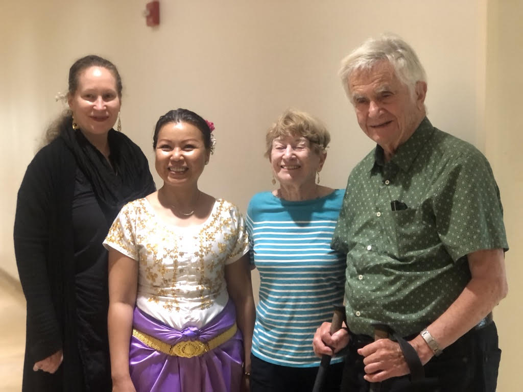 4 people stand side by side, smiling into the camera against a white wall.