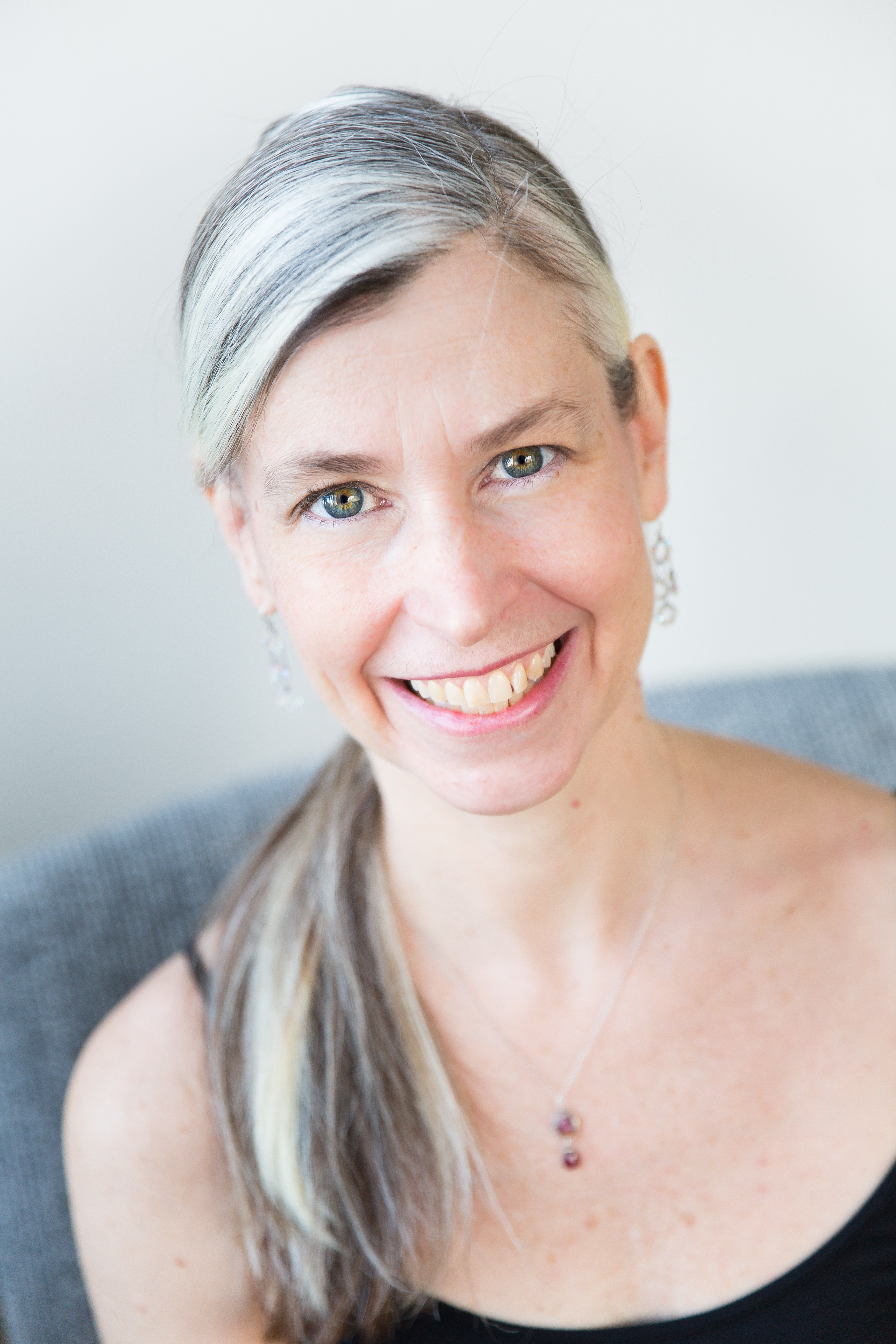A headshot of Heather, smiling, a white woman, with her gray and black hair in a pony tail. She is wearing a black tanktop.