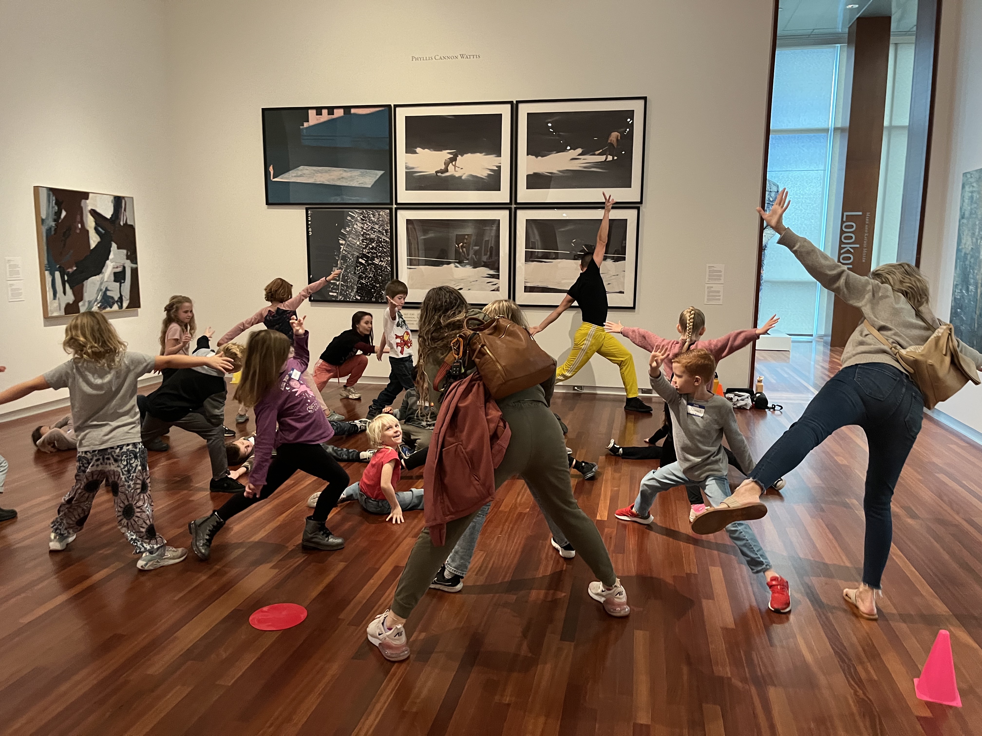 A group of young students and two older teachers create shapes in an art gallery