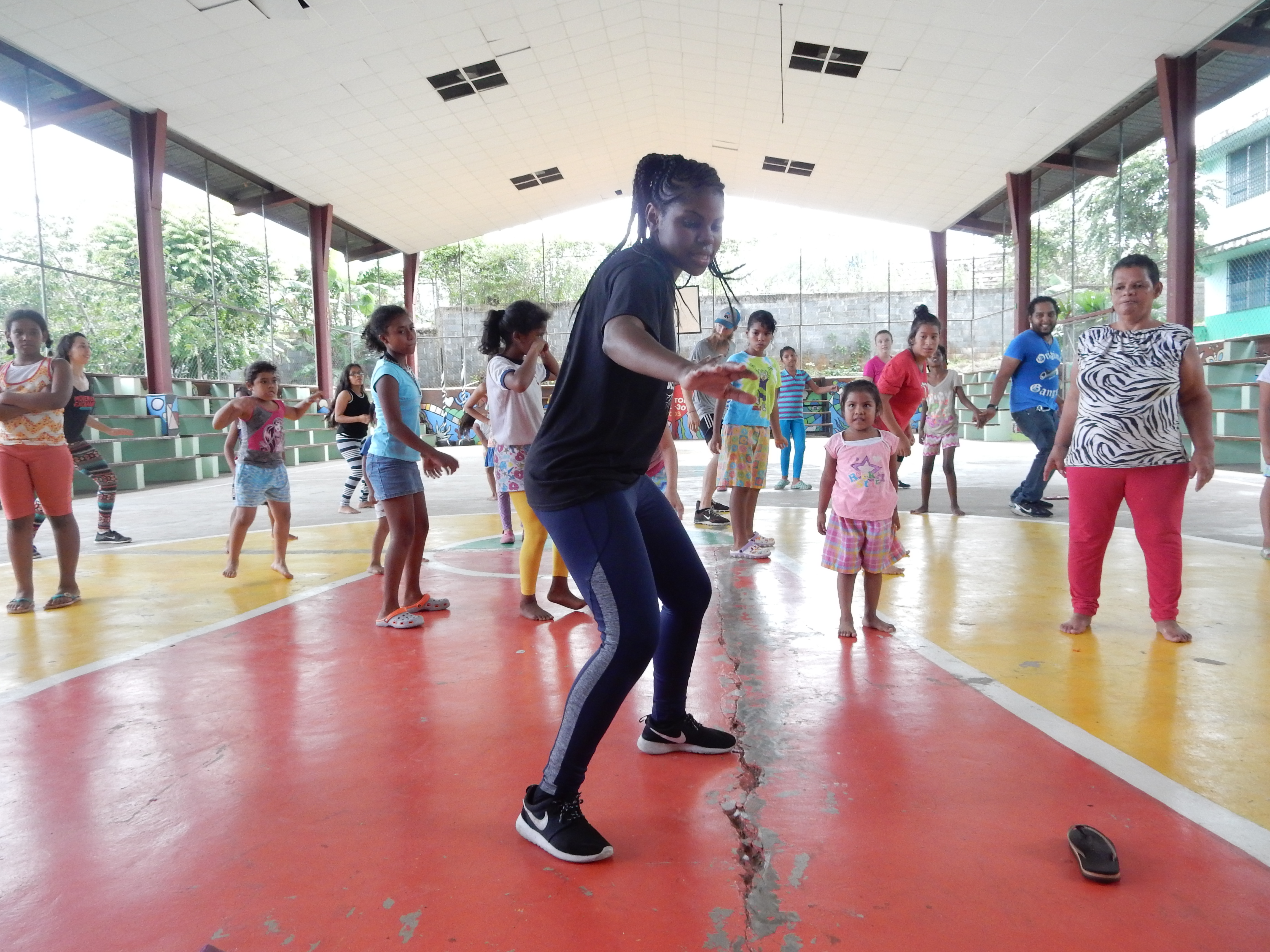A group of students randing in age from small children to grown adults, in colorful clothes, take class in a gym setting in Panama.