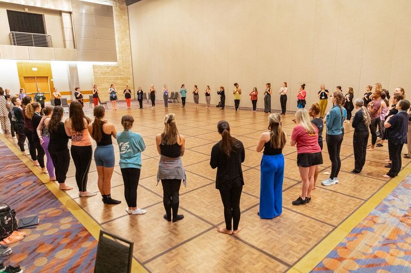 a large group of dance teachers standing in a circle at the 2023 national conference