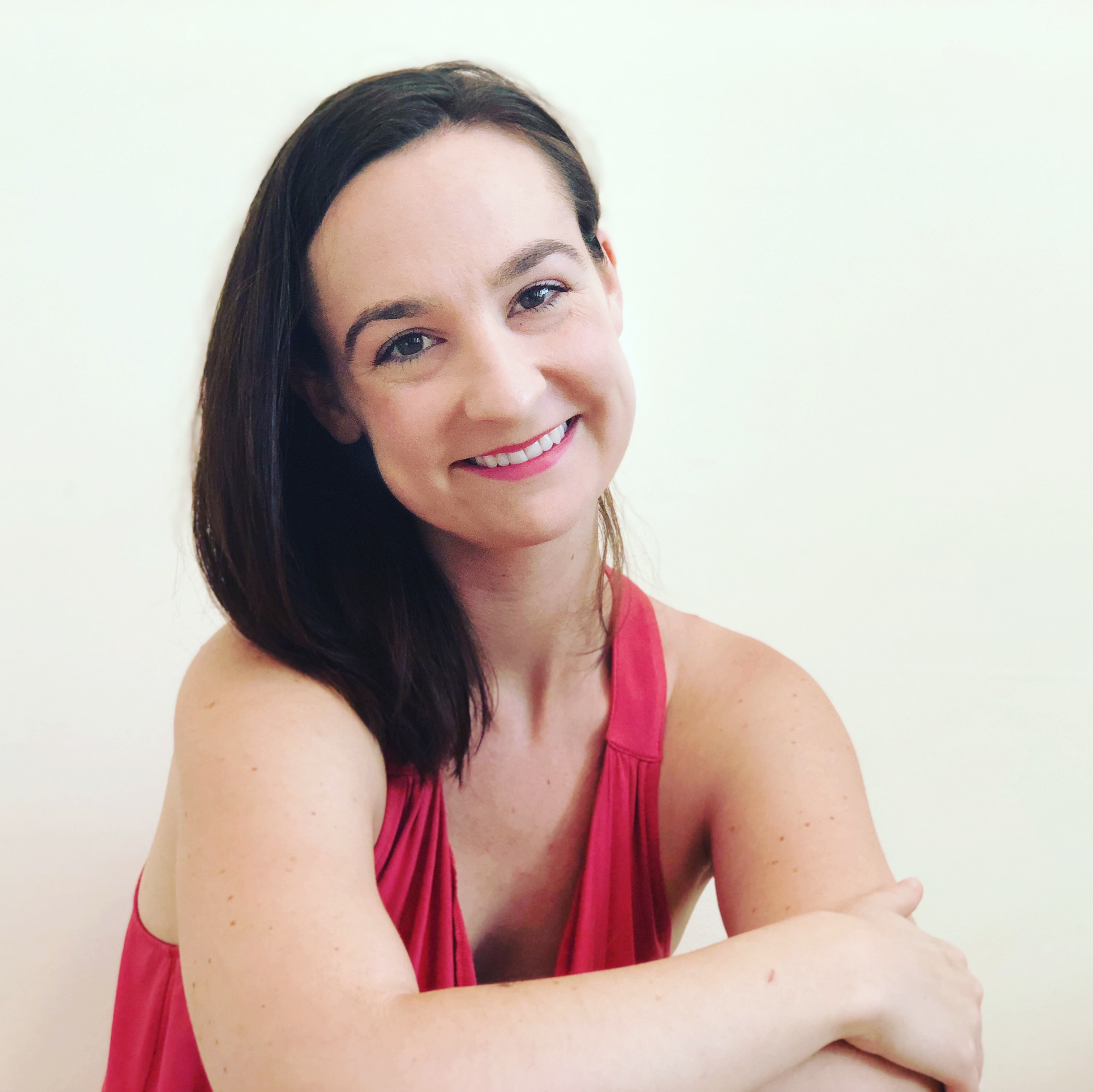 Lydia Hance headshot, a white woman with dark brown hair wearing a pink tank top smiling against a white back round.