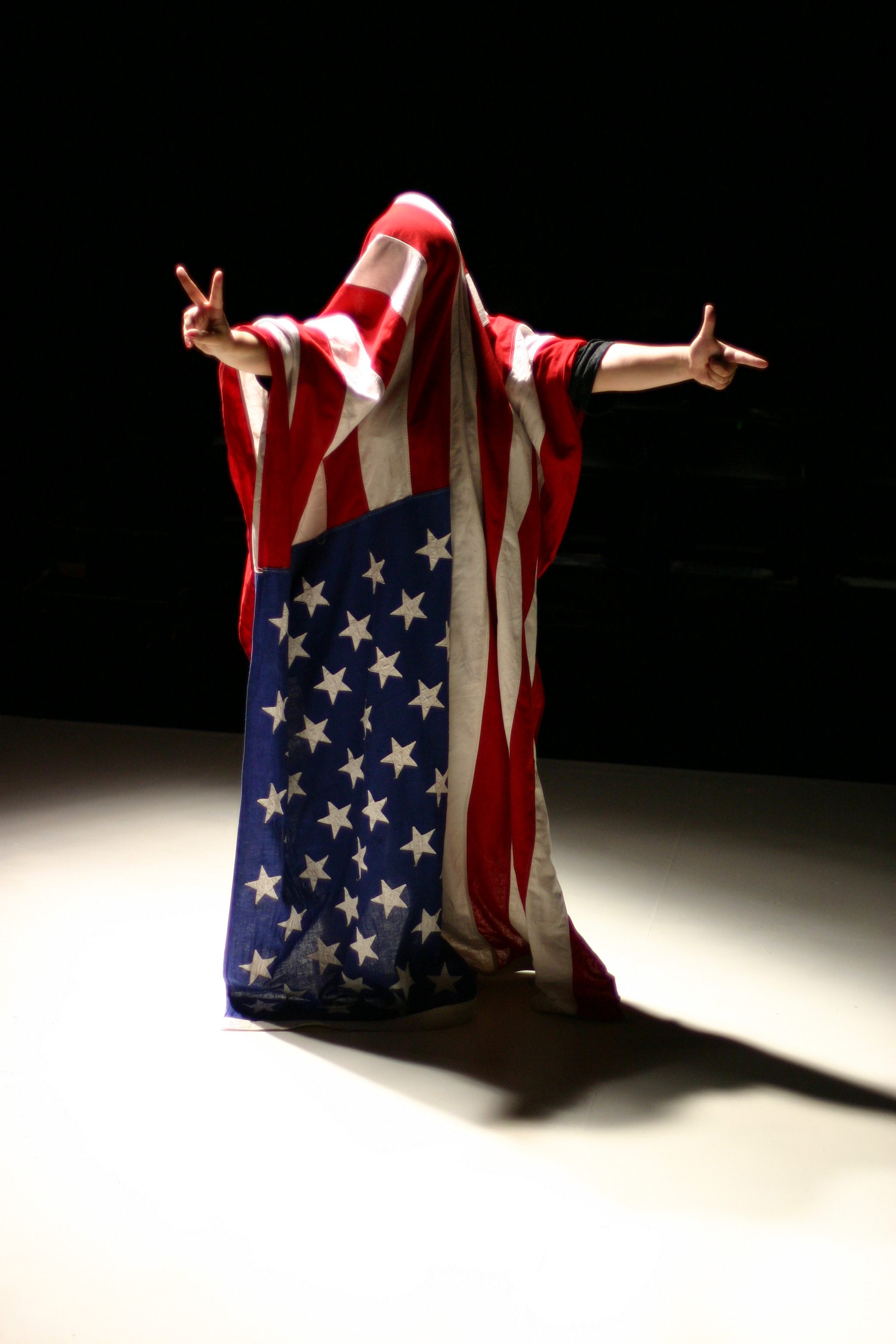 A person with an American flag draped over them.  Holding one hand on the left in a finger gun and the other hand in a peace sign.