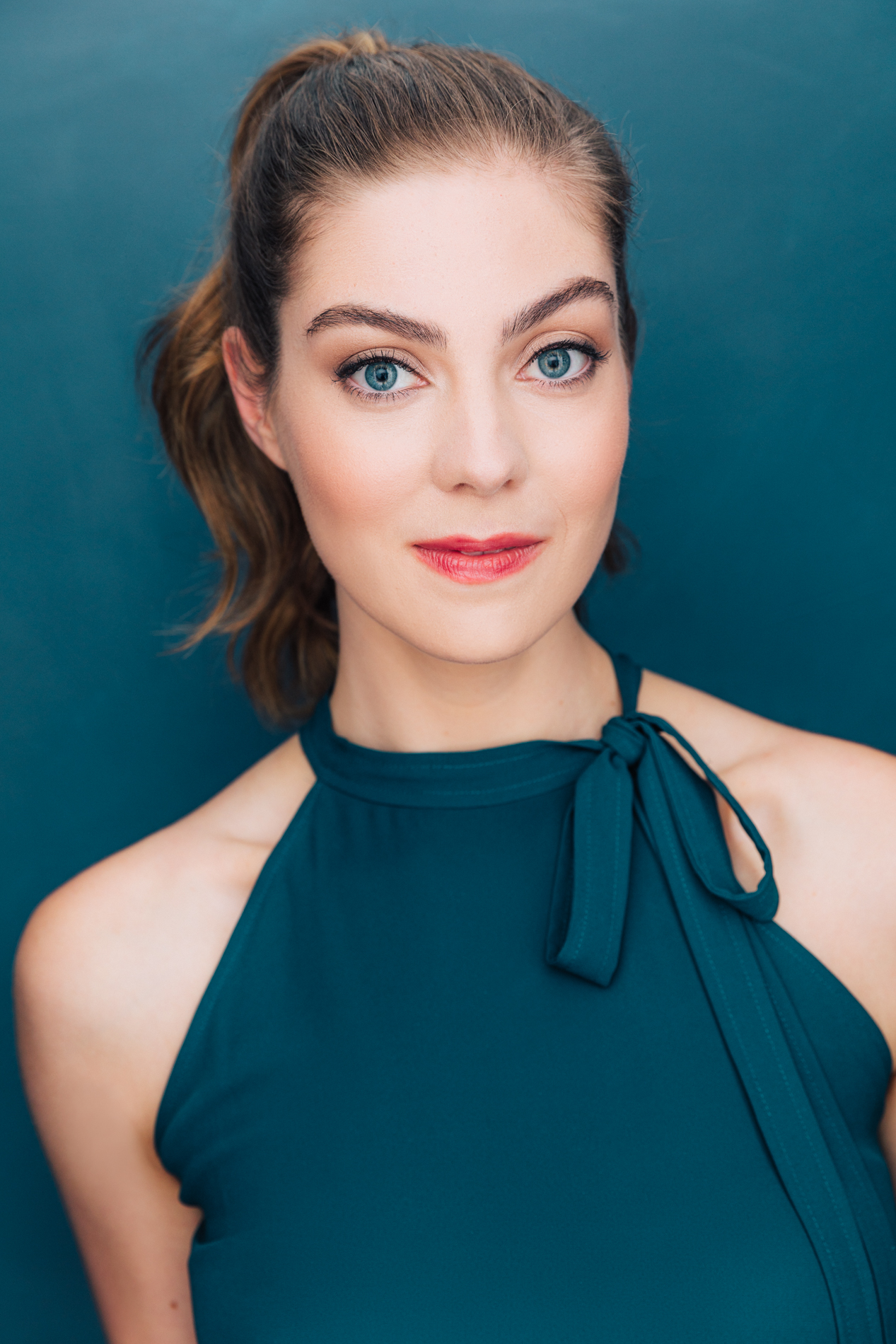 Headshot of Natasha, a white woman with blue eyes and brown hair in a high pony tail. She is wearing a turquois tank top and the backround is also turquois.