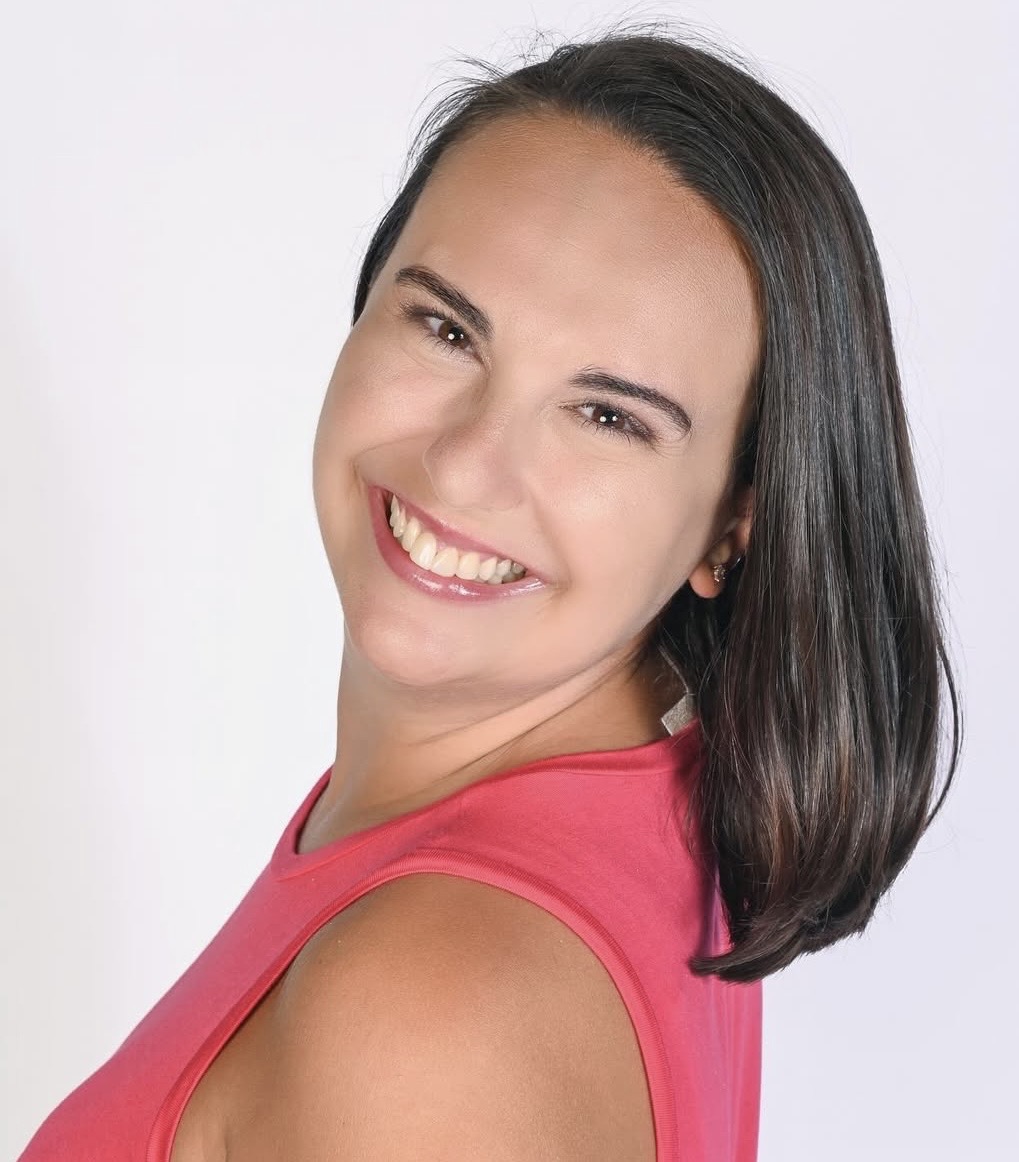 Headshot of Cassidy, a white woman with short dark brown hair. She is wearing a pink tank top, looking over her shoulder smiling at the camera.