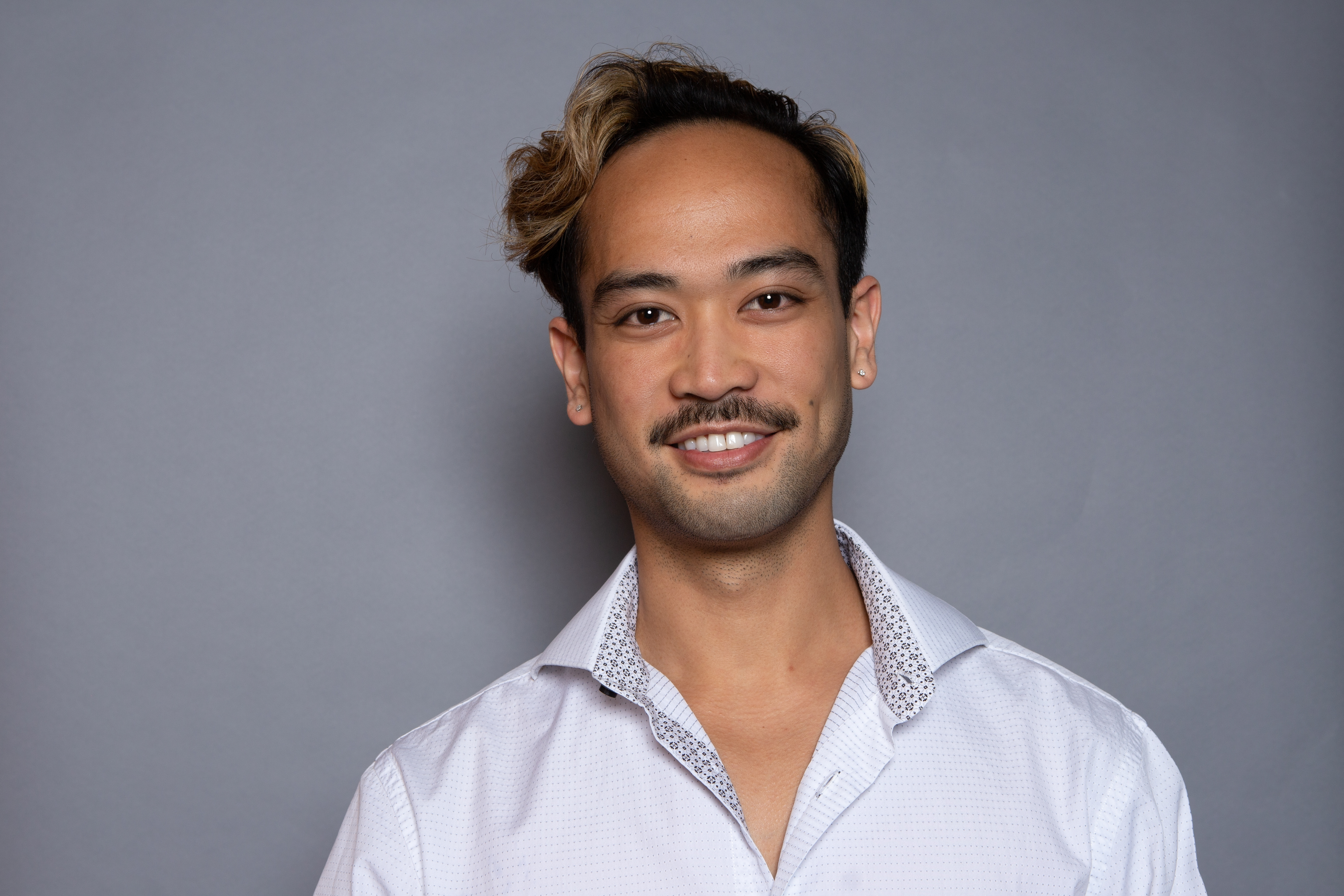 Dr. Joshua Honrado is wearing a white button up shirt and smiling, with short dark hair and facial hair